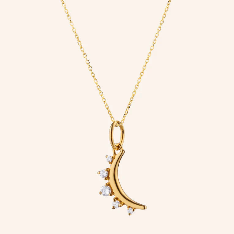 Gold necklace with a crescent moon pendant on a light beige background