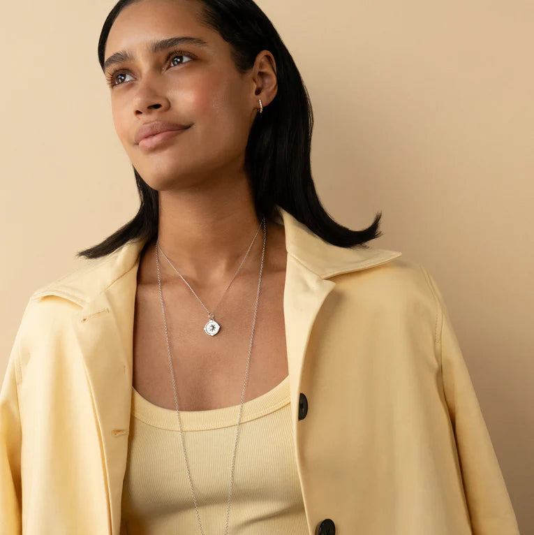 Woman wearing a beige coat and dress with a necklace against a beige background