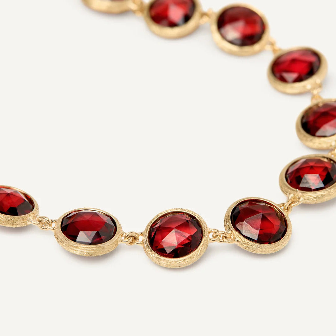A close-up of a gold chain necklace featuring oval-cut, faceted deep red garnet gemstones in gold bezel settings, set against a clean white background.