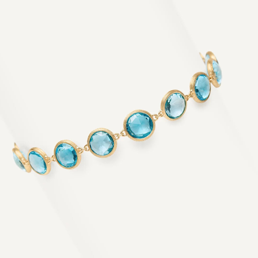 A delicate gold chain bracelet featuring blue topaz gemstones, displayed on a clean white background.