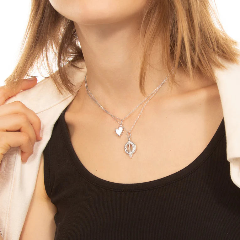 Woman wearing a necklace with heart and oval pendants on a plain background