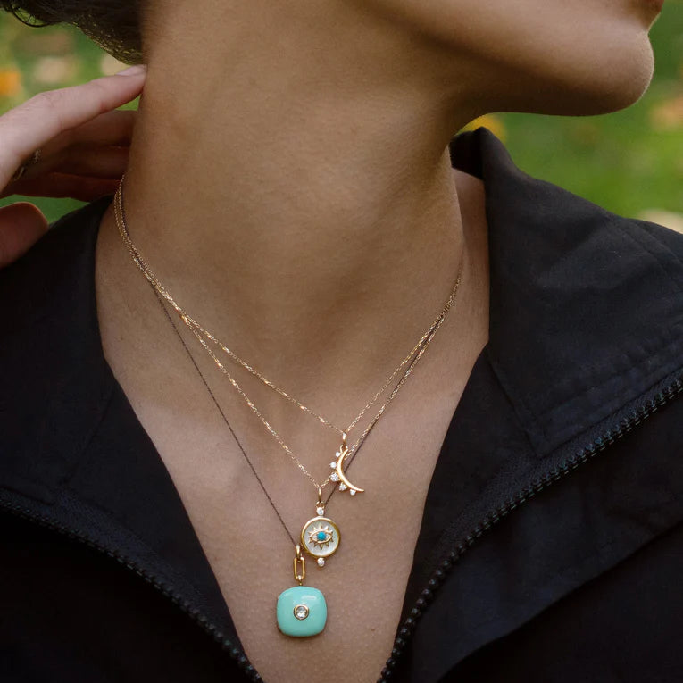 Close-up of a person wearing a gold necklace with a turquoise pendant.