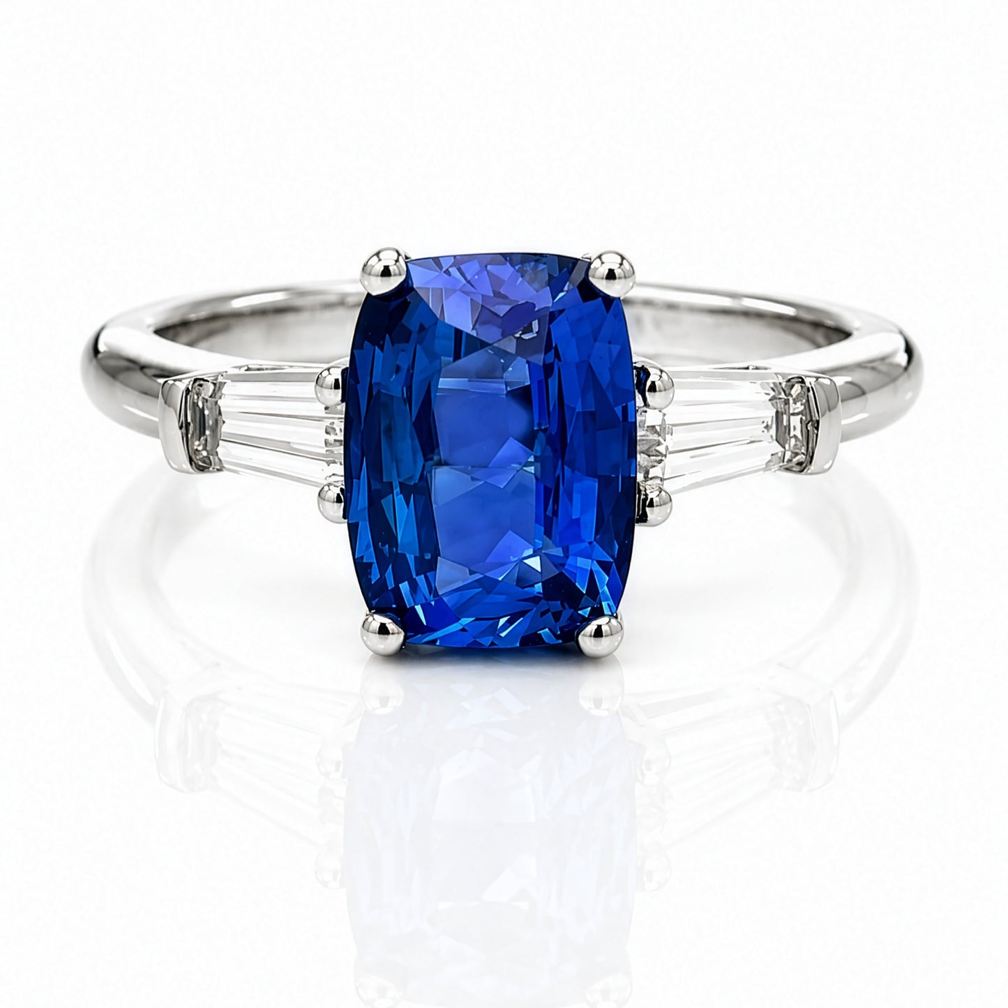 A platinum ring featuring a large elongated cushion-cut blue sapphire center stone, accented by tapered-baguette diamonds on each side of the band, set against a clean white background with a soft reflection.