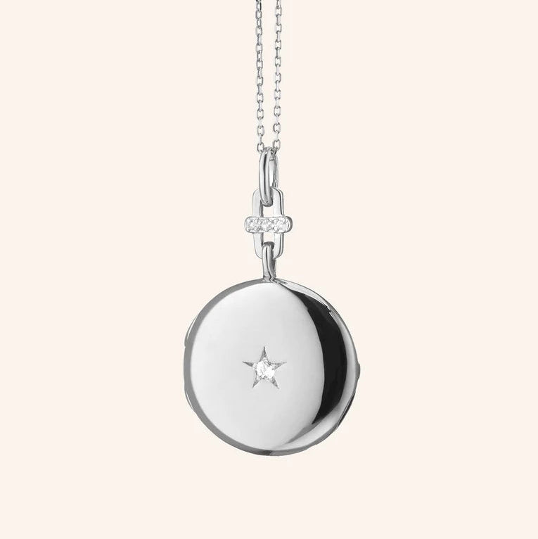 Silver necklace with a round pendant and star detail on a light beige background