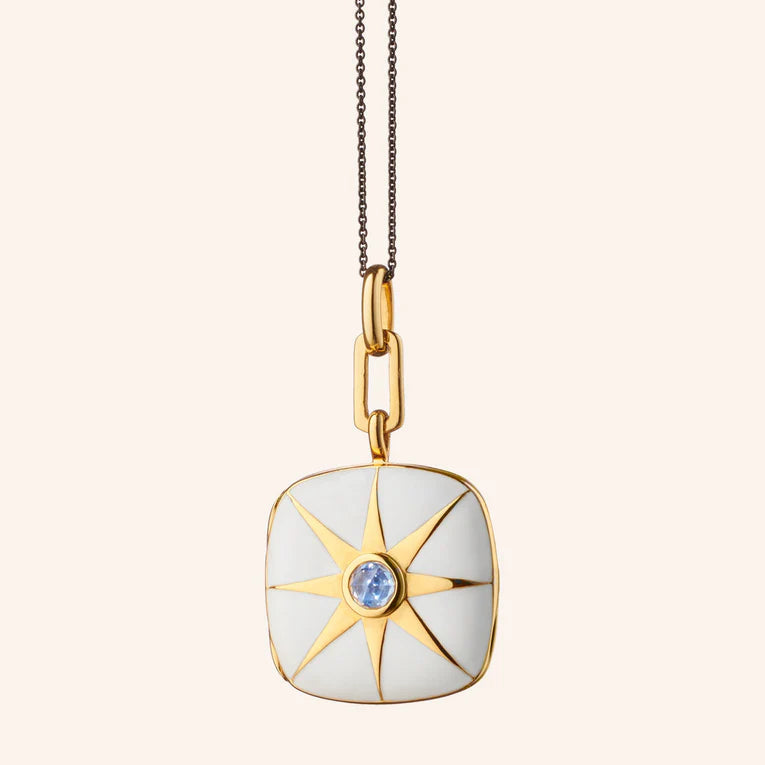 Gold and white pendant necklace with a blue gemstone on a light beige background