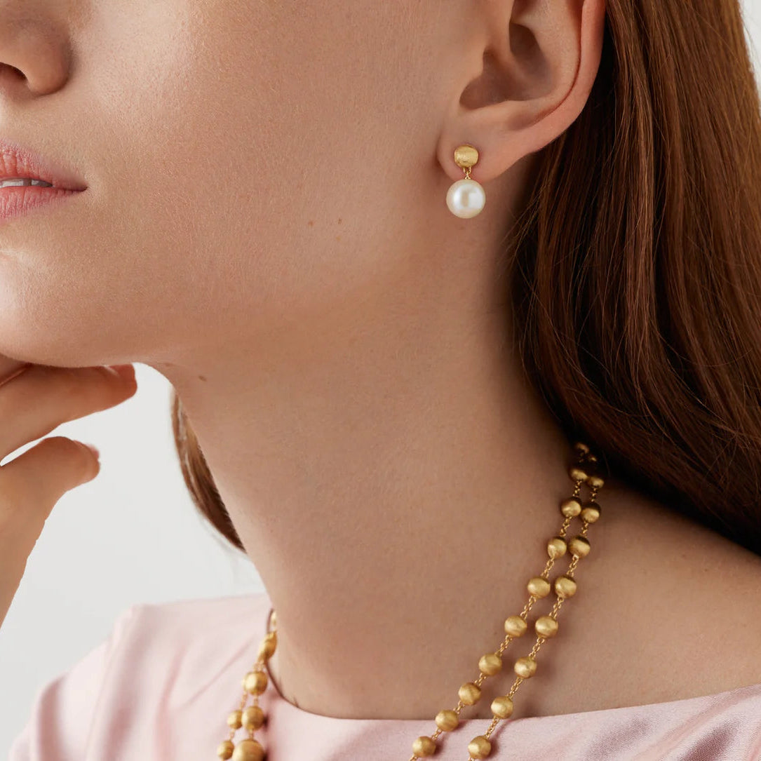 Close-up of a person wearing gold necklace and pearl earrings on a light background