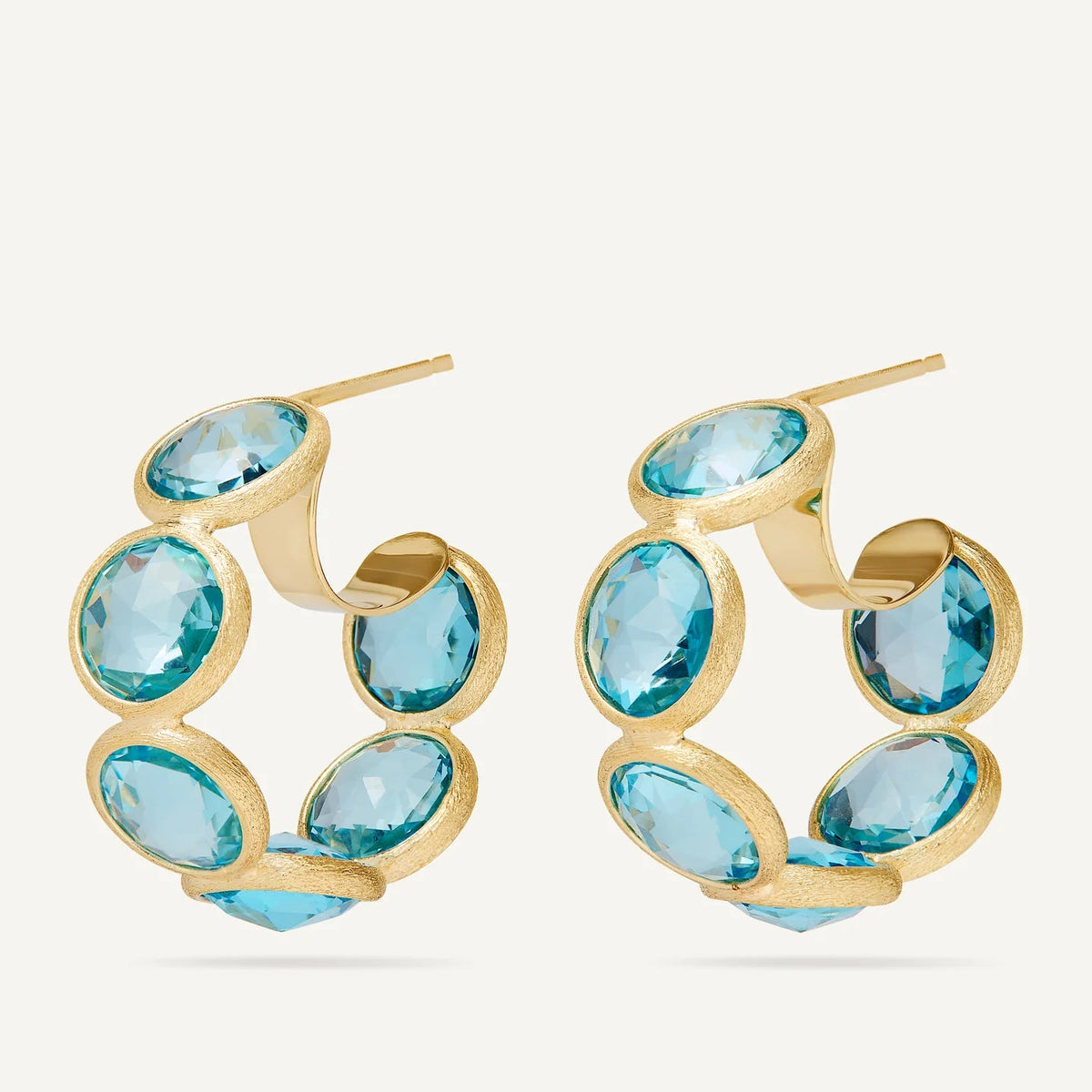 A pair of gold hoop earrings featuring multiple bezel-set blue topaz  gemstones, displayed on a clean off-white background.