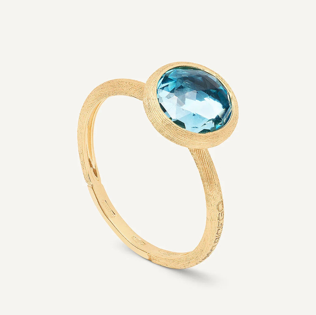 A gold ring featuring a bezel-set round-cut light blue topaz gemstone, shown on a clean off-white background.