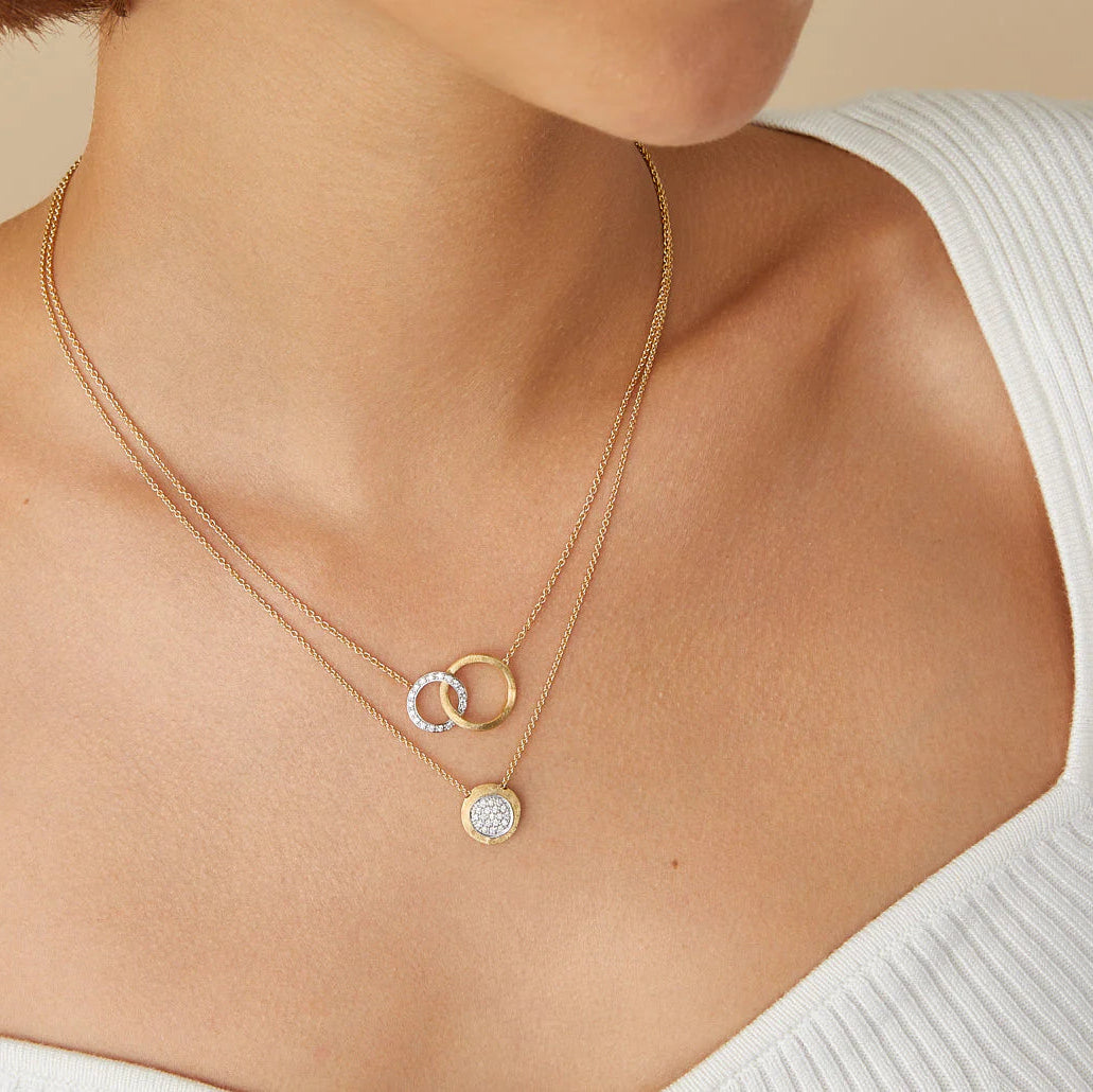 Gold necklace with circular pendants on a person wearing a white top against a beige background