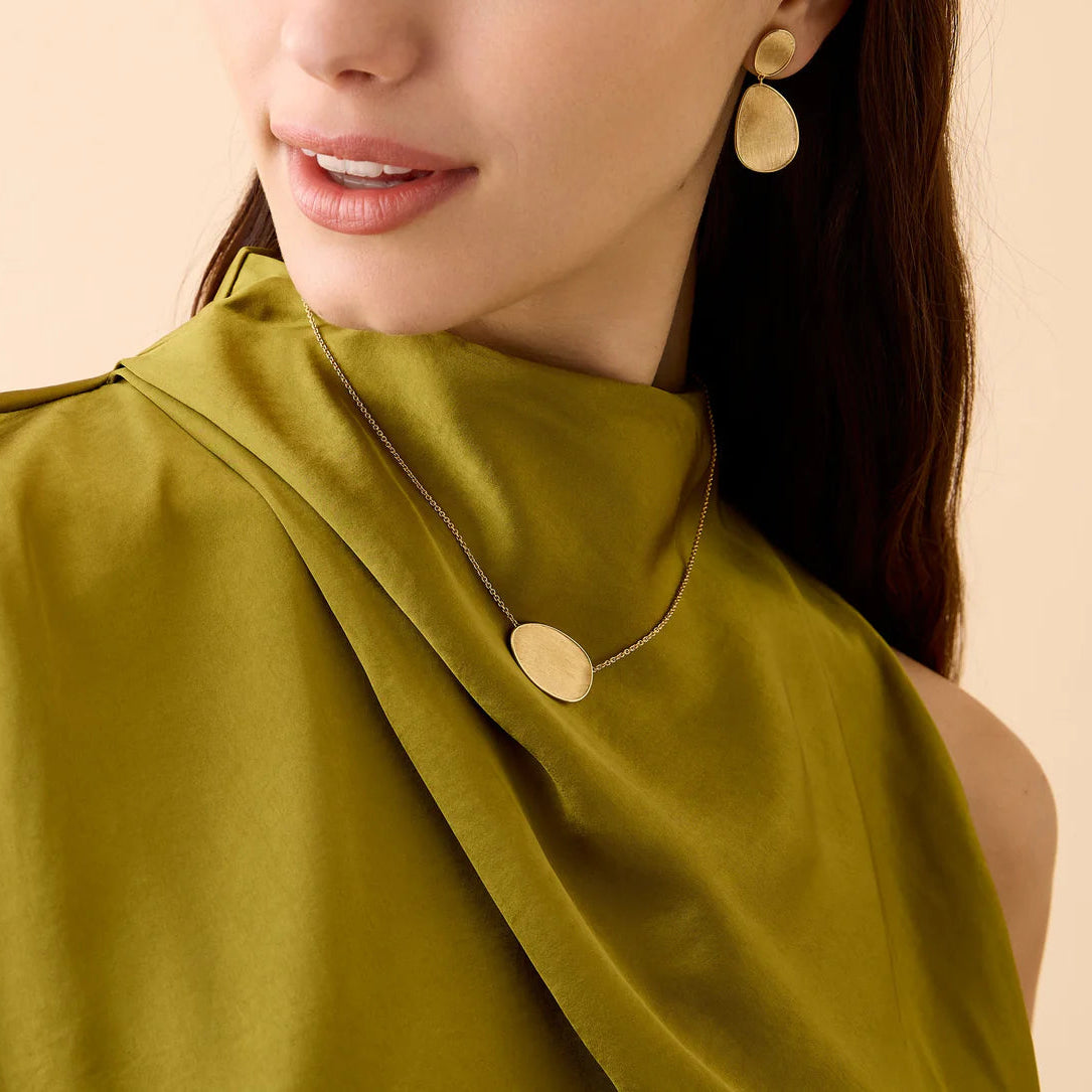 Woman wearing a green sleeveless top with gold buttons and matching earrings on a beige background