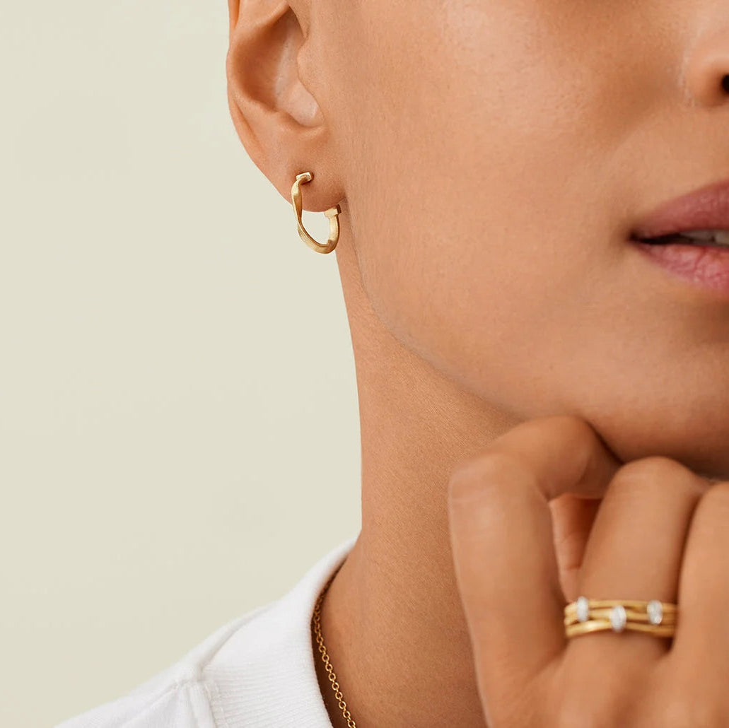 Close-up of a person wearing gold hoop earrings and a ring on a neutral background