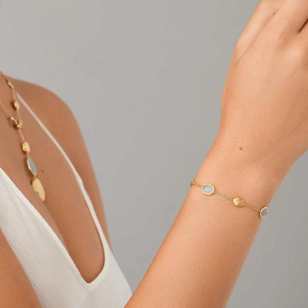 Gold necklace and bracelet on a person against a gray background