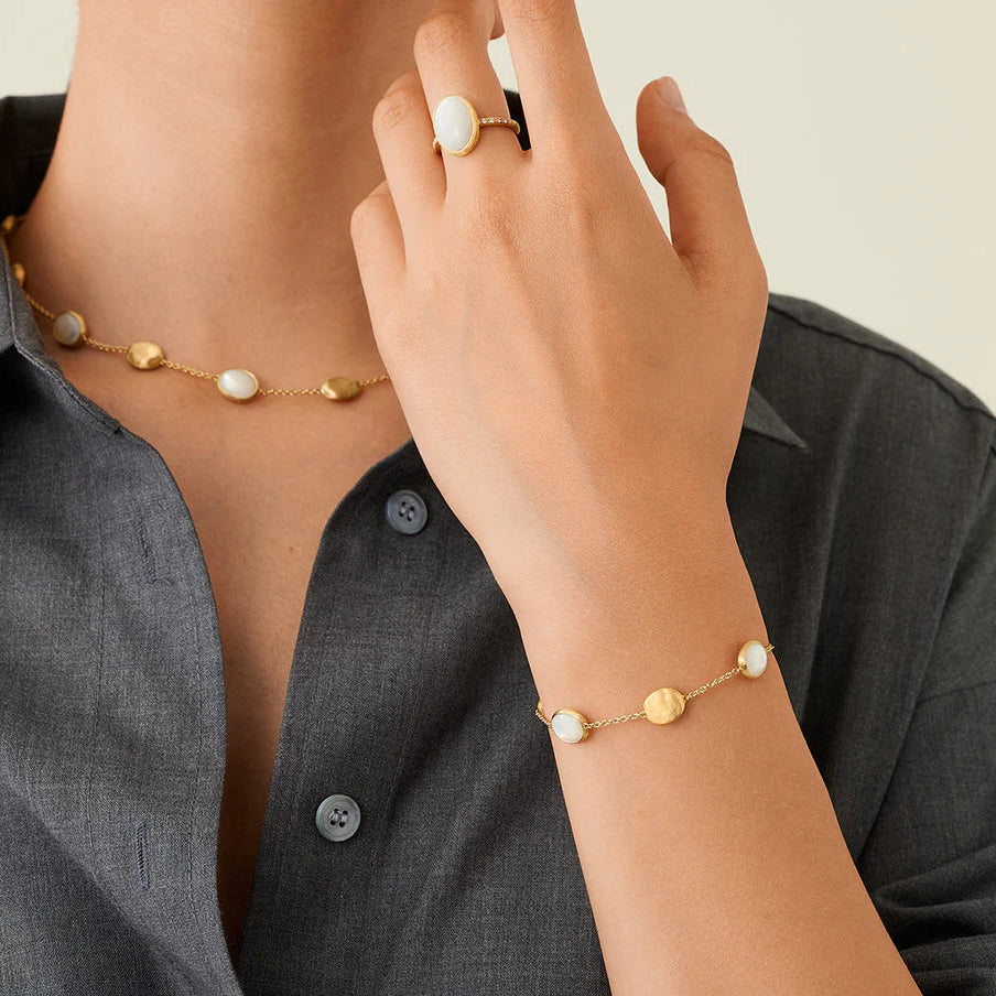 Person wearing a gold bracelet and ring with small stones on a neutral background