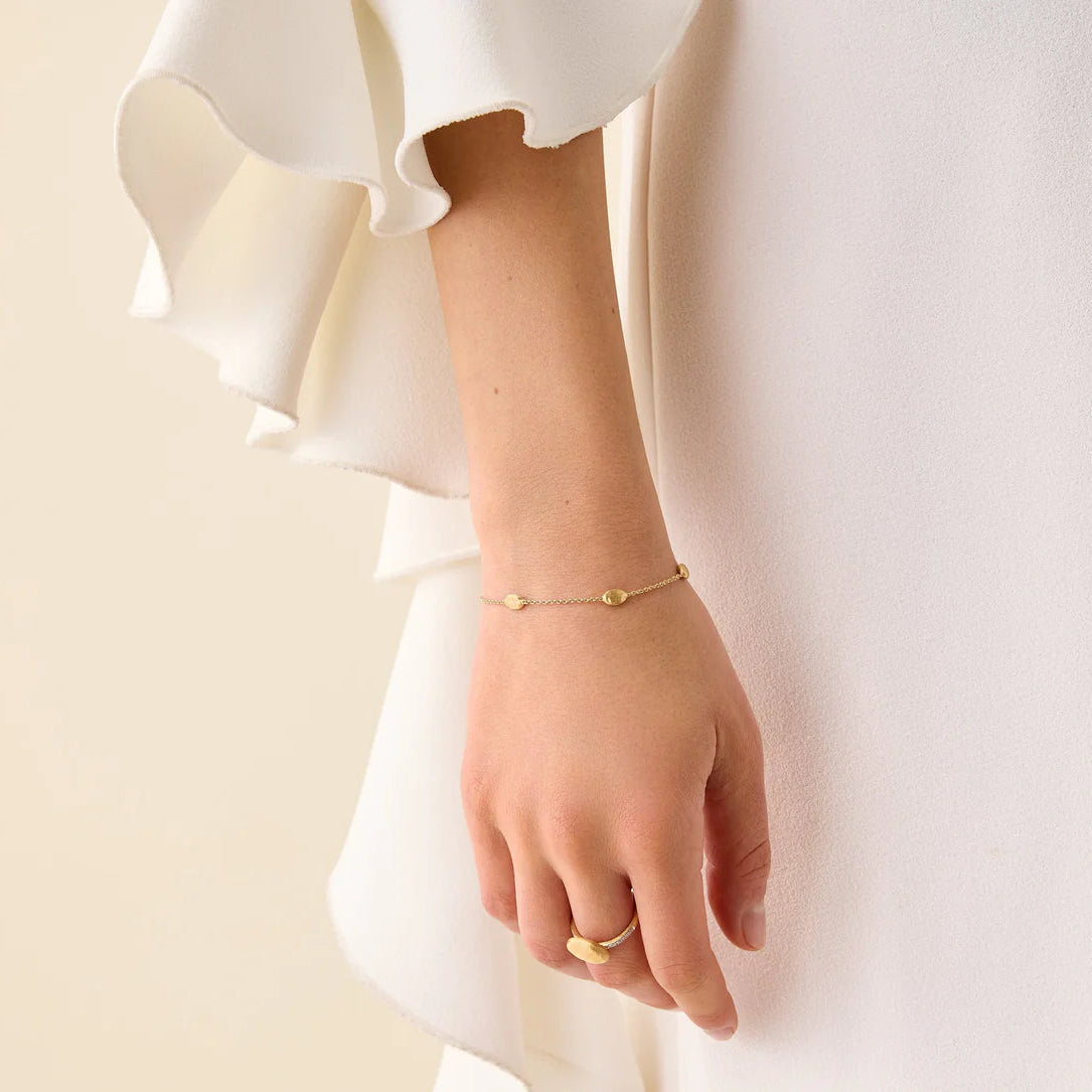 Close-up of a person's wrist wearing a gold bracelet and ring on a plain background